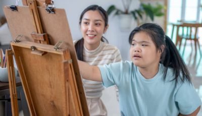 A young art teacher woman helps autistic children to paint on canvas.
